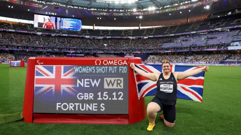 A female athlete posing to a photo next to a screen with her world record