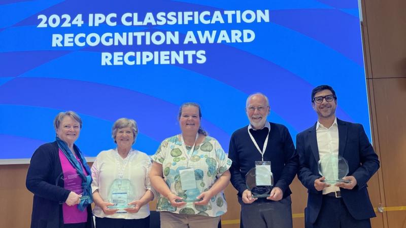 Five recipients pose for a photograph in front of a screen that says "2024 IPC Classification Recognition Awards Recipients"