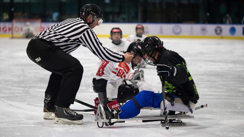 A Para ice hockey official dropping the puck in front of two players