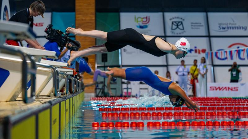 Two female Para swimmers jump in the water in a swimming pool
