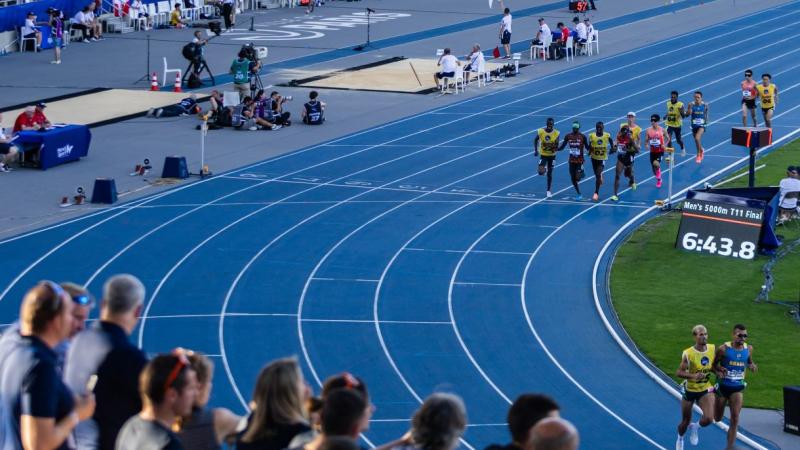 A group of men running with guides in an athletics stadium
