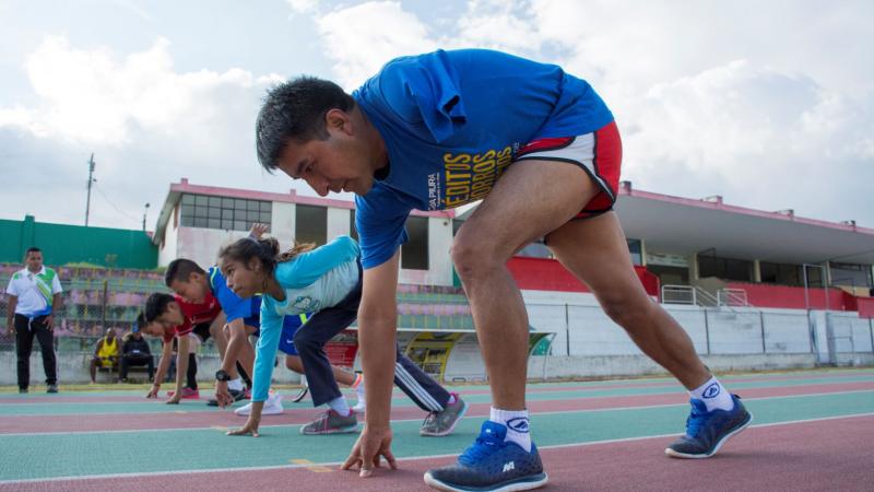 Five boys and girls with disabilities are bending down at the start line before racing at an outdoor track