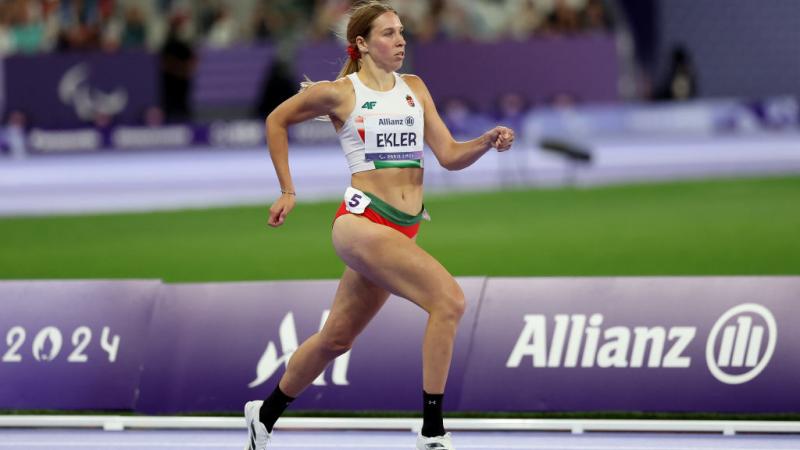 A female Paralympic sprinter competing at Paris 2024. Her bib has the logo of Allianz