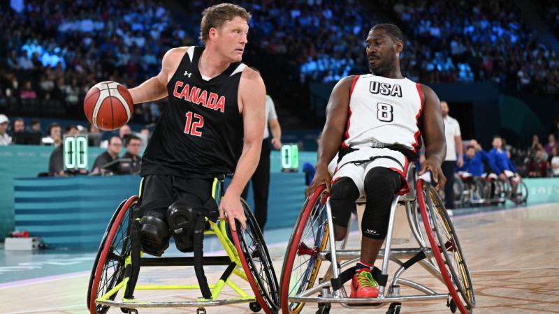 Two male wheelchair basketball players in action. The player in the left is dribbling the ball
