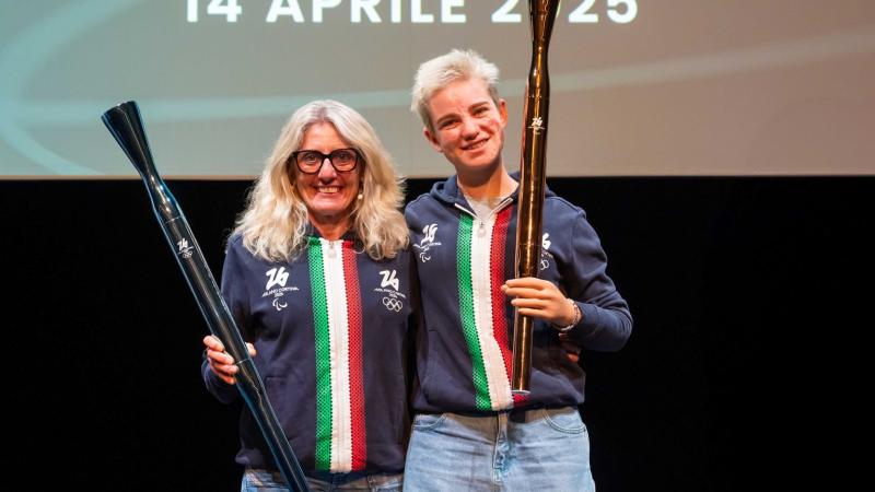 Bebe Vio and Stefania Belmond are holding the Milano Cortina 2026 torches during a presentation event. 