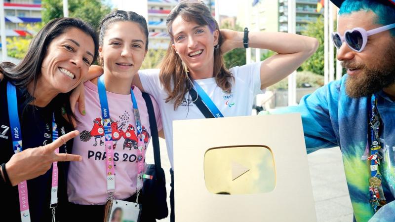 One male and three female athletes are posing with the golden plaque that is awarded to YouTube accounts with more than 1 million subscribers