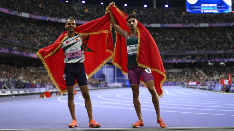 Two men with the Moroccan flag celebrating on the Stade de France athletics track