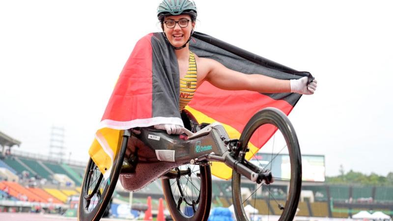 A female wheelchair racer celebrates on the track, holding the German flag