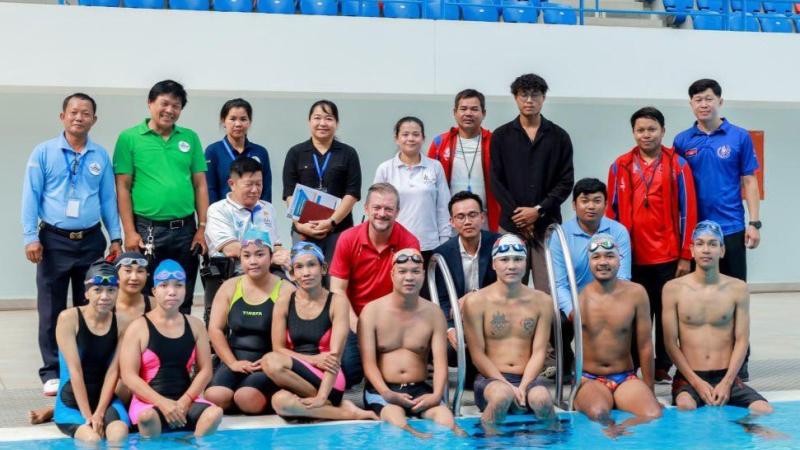A group photo of about 20 people including swimmers and officials by the pool