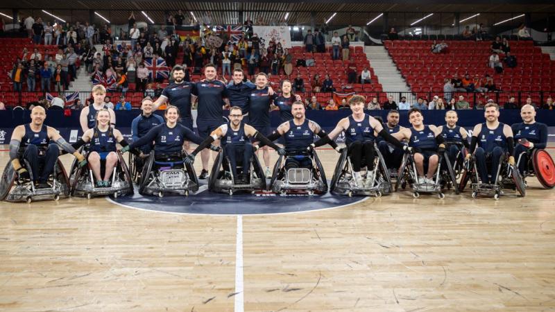 Seventeen people, including wheelchair rugby players and staff, pose for a group photo on a court