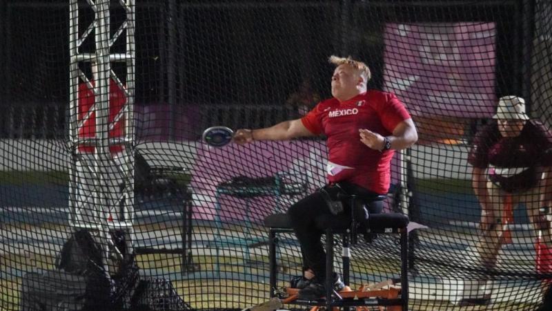 A female seated thrower competing observed by an official