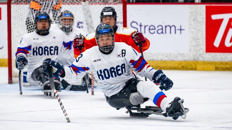 A Korean Para ice hockey player watched by three other players on ice