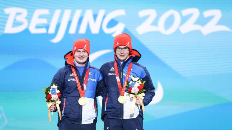 Two male athletes pose for a photograph on the podium after receiving gold medals
