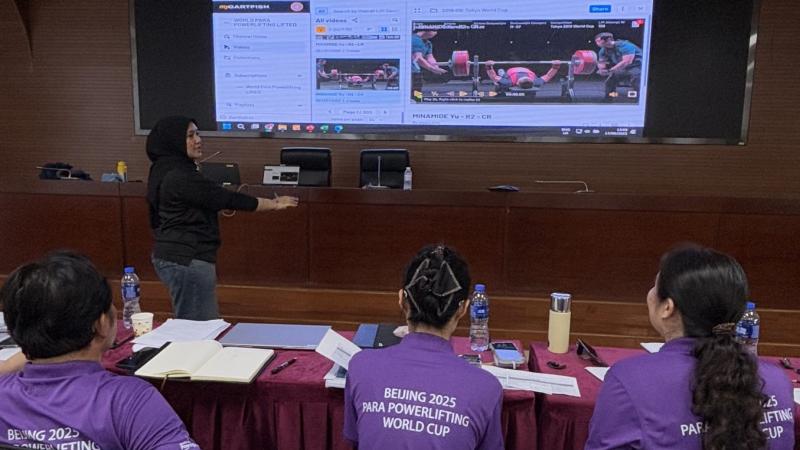 Three participants watching a woman make a presentation on a screen