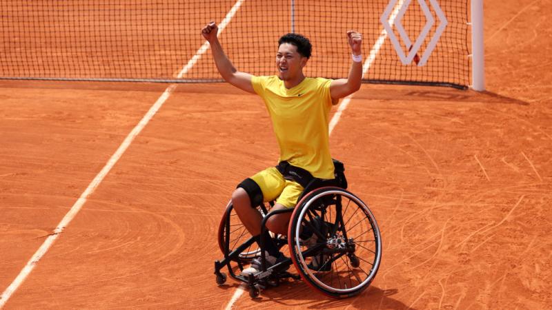 A male wheelchair tennis player celebrates after winning match point on clay court