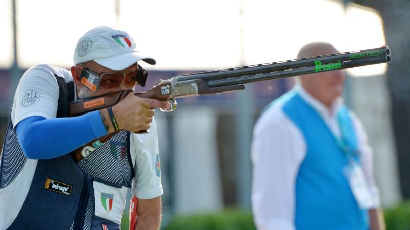 A male trap shooter observed by an official during competition