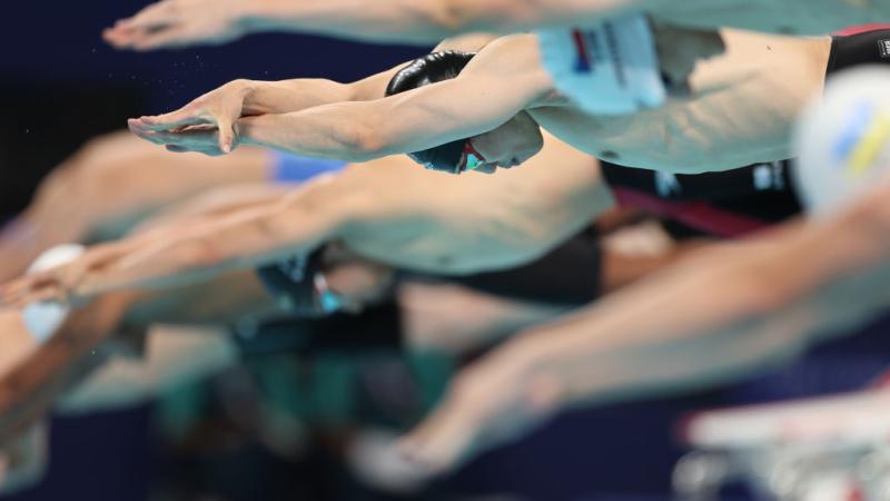 A group of male swimmers jumping into the pool at the start of a race