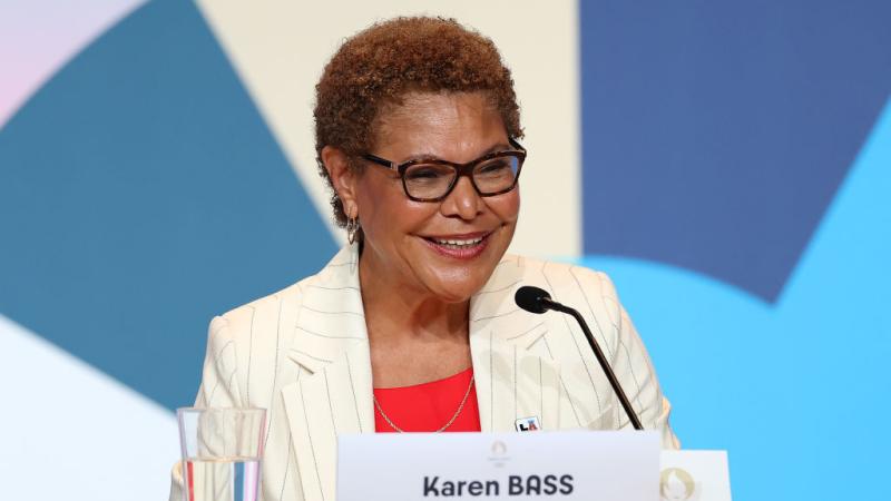 Mayor Karen Bass speaks during a Paris 2024 press conference. She is sitting in front of a mic and a name tag