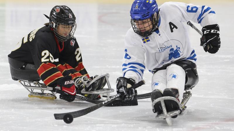 A Canadian player challenging a Team World player in a women&#039;s Para ice hockey game