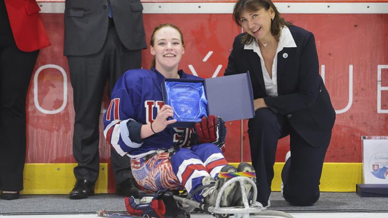 A female Para ice hockey player receiving an award next to a woman on the ice