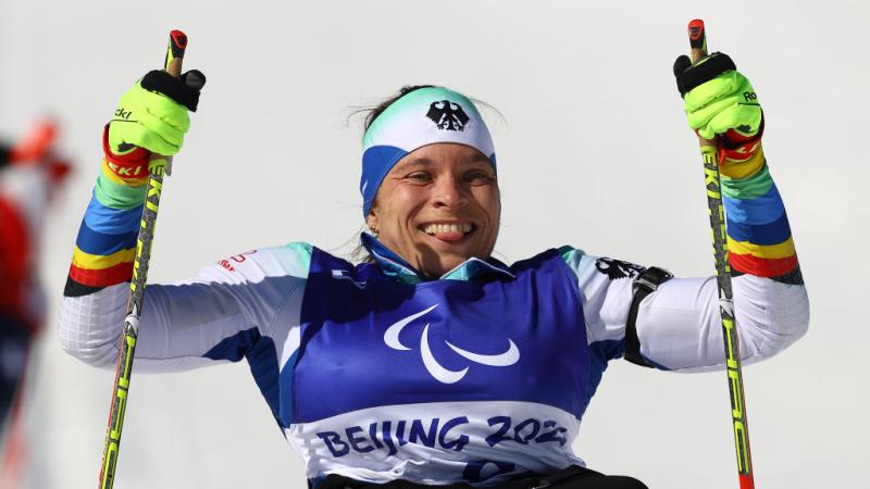 A female Para biathlon athlete smiles and she is holding two ski poles