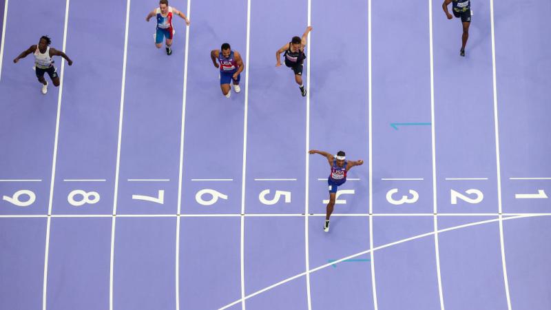 A photo taken from above shows purple athletics track and six athletes racing