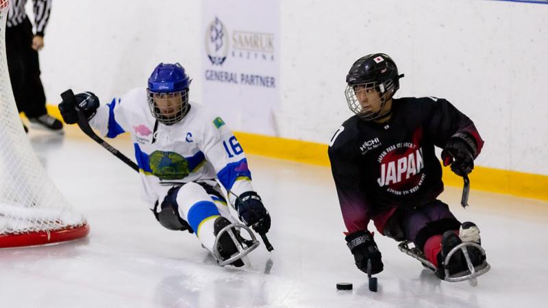 A Japanese Para ice hockey player with the puck with a Kazak player behind him