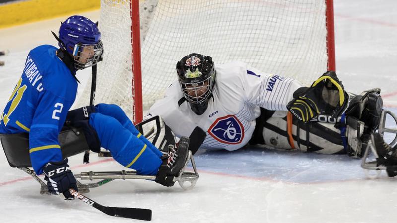 A male Para ice hockey player taking a shot in front of the goaltender