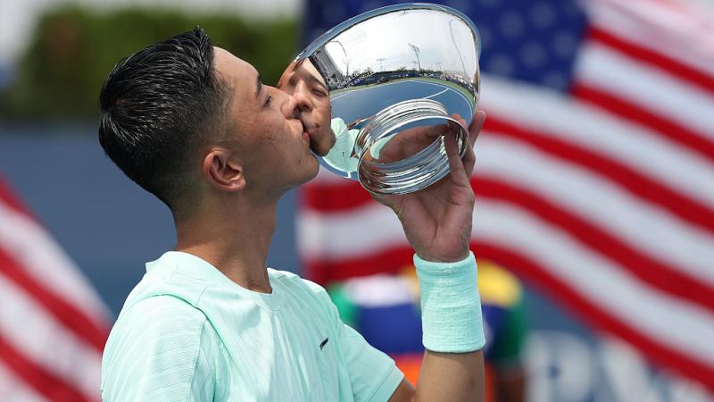 A male wheelchair tennis player is kissing a silver trophy