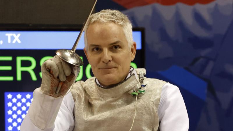Scott Rodgers smiles for a photo while holding an epee