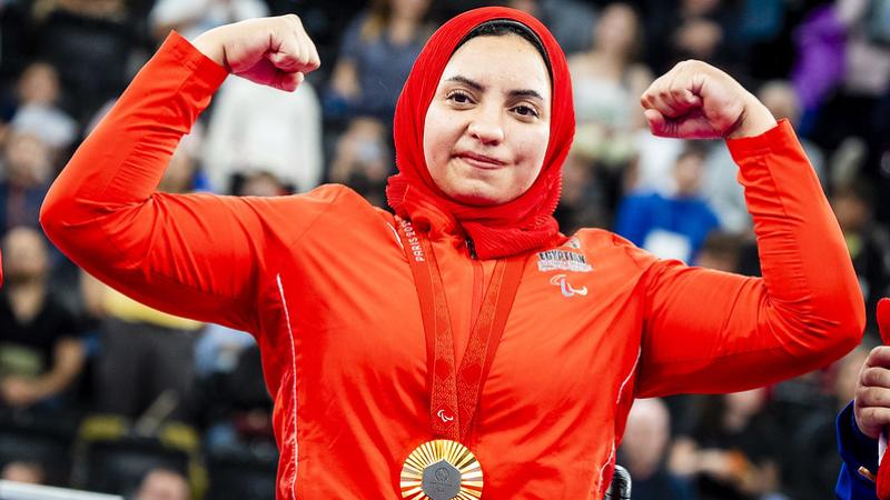 A female athlete with a gold medal flexing her arms 