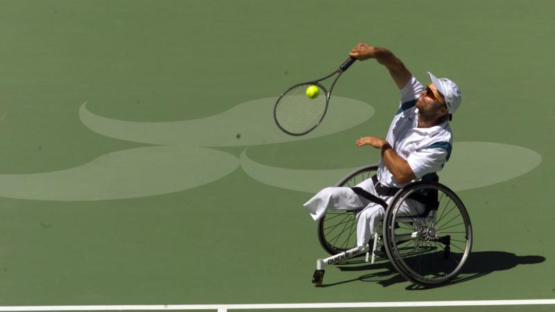 A male wheelchair tennis player is in competition on a grass court