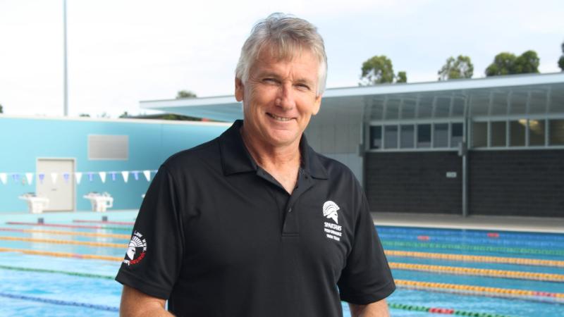 Professor Brendan Burkett is posing for a photograph in front of an outdoor pool