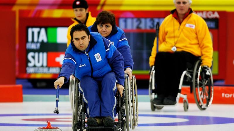 A male wheelchair curling athlete is delivering a stone with a stick during competition at Torino 2006.