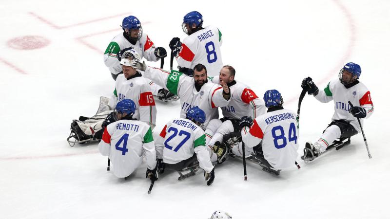 Nine Para ice hockey players wearing Italy&#039;s white jersey are celebrating on ice