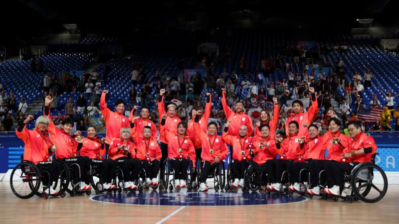Eighteen wheelchair rugby players and officials wearing a red jersey pose for a photograph after receiving gold medals