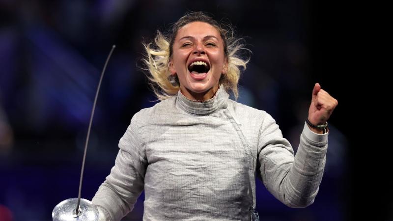 A female athlete smiling and pumping her fist following a wheelchair fencing competition