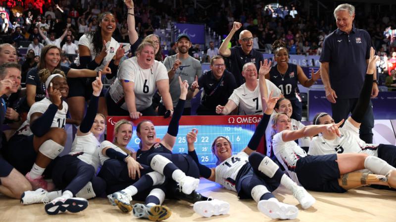 Female sitting volleyball players are celebrating in front of a scoreboard at the Paris 2024 Paralympic Games