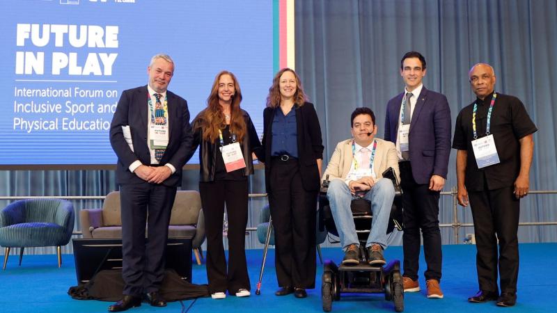 Six people pose for a group photo in front of a screen that says &quot;Future in Play&quot;