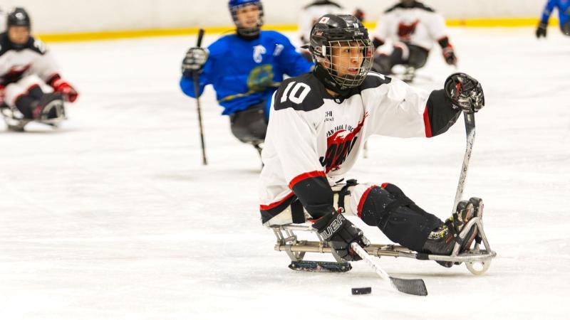 A male Para ice hockey wearing a white jersey is in action