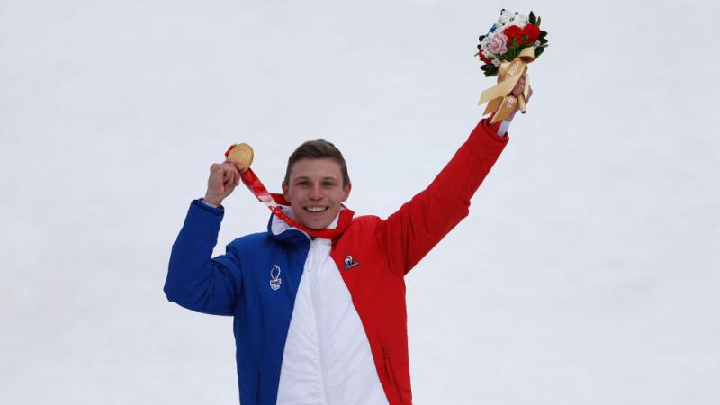 A male athlete wearing France's blue, white and red uniform celebrates on the podium at the Beijing 2022 Paralympics