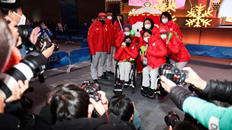 Nine athletes and officials from the Japanese delegation pose for a group photo in front of photographers at Beijing 2022