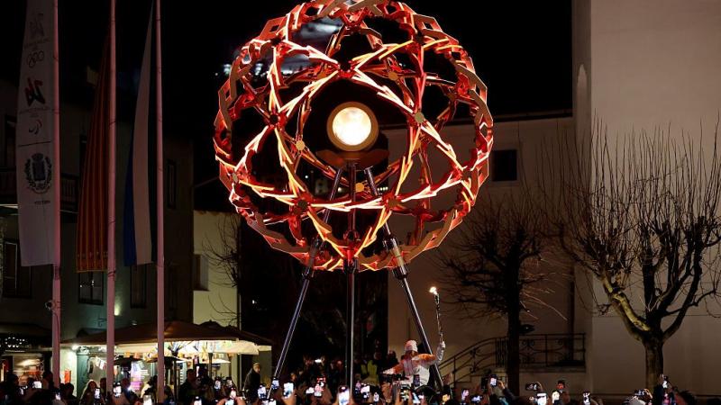 A sphere-shaped cauldron is located in the middle of a city, surrounded by people taking photos on their smartphones