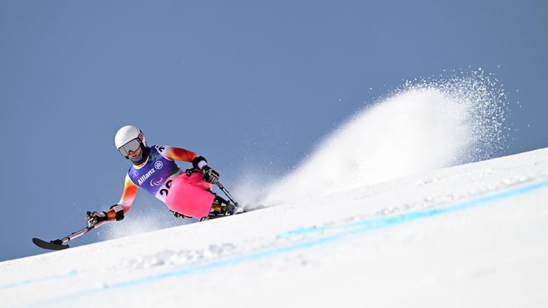 A woman in a pink sit-ski takes a downhill bend