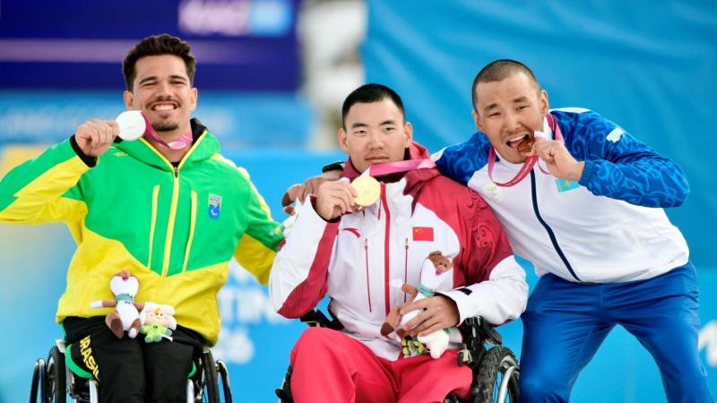 Three athletes in a wheelchair pose for a photo on the podium