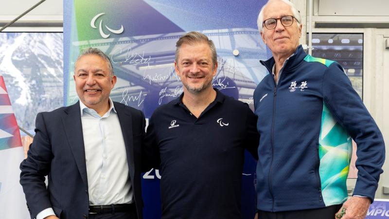 Three male officials are posing in front of a purple mural