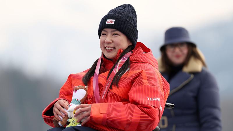 A female Para alpine skier wearing a red uniform is smiling