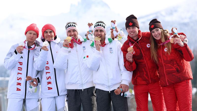 Six athletes are posing for a photo on the podium at the Milano Cortina 2026 Paralympic Winter Games