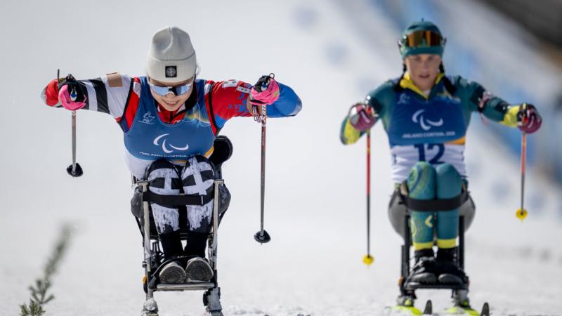 Two female sit-skiers race side by side