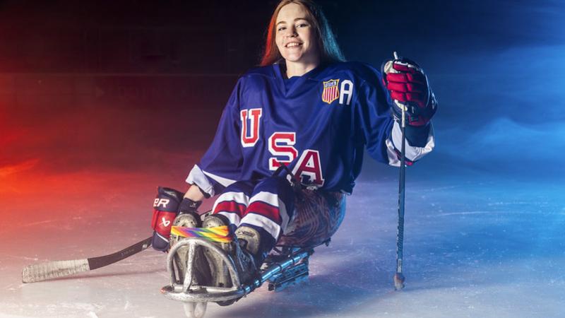A female Para ice hockey player on ice smiling while posing for a picture